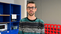 un homme à lunettes debout devant une étagère bleue.